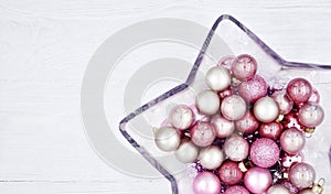 Star shaped glass vase with Christmas balls on a wooden white background.