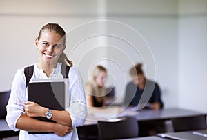 Star student. A teenage girl holding her laptop while standing in the classroom.