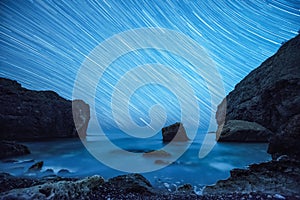 Star trails above the rocky seashore.