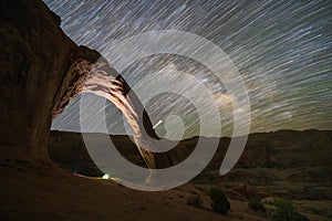 Star trails behind Corona Arch and a lit tent