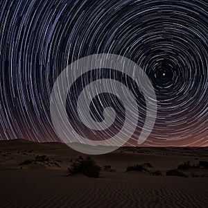 Star trails form circular patterns in the night sky above a desert landscape. The