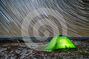 Star trails in winter at night over a tent on a mountain top