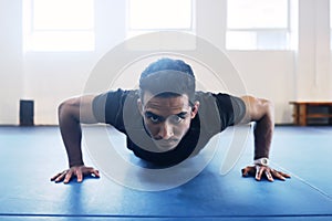 Stare the push up beast in the eyes. a young man doing pushups as a part of his workout routine at the gym.