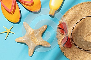 Starfish, beach slippers, sun cream, sunglasses and a hat on a blue background