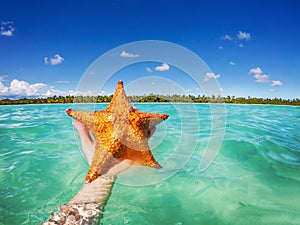 Starfish in hand, Caribbean sea and beautiful tropical island as background. Punta Cana, Dominican Republic