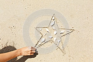 Starfish, seashells on the sand. Creative top view. Copy space. Children`s hand creates a drawing summer day.