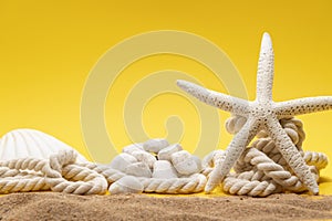 Starfish, shell, stones and rope on a plain yellow background and sand