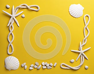 Starfish, shells, stones and rope on a plain yellow background