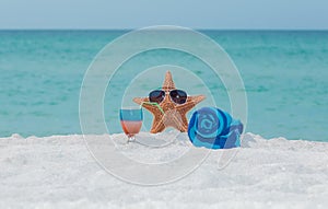 Starfish , towel and cocktail on white sand tropical beach