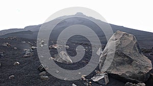 Stark and desolate volcano creater landscape with black lava sand and rocks and other craters behind