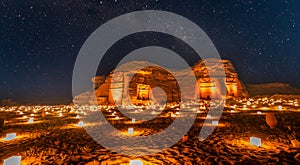 Starlight sky over the ancient nabataean tombs of Hegra city illuminated, night panorama, Al Ula, Saudi Arabia