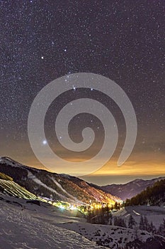 Starry sky above snowy winter mountains, ski resort town