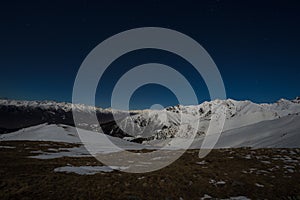 Starry sky night view on the Alps. Snow capped mountain range in moonlight.