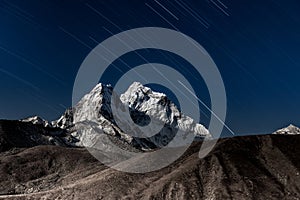 Stars falling above Ama Dablam mountain peak lit.