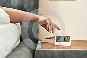 Start of the day. Close up of hand of woman reaching snooze button on digital alarm clock in early morning