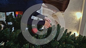 Start of decorating the tree on Christmas Eve. Young woman holding a golden globe hangs it on the fir branch in front of fireplace