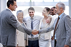 The start of a great working relationship. two businessmen shaking hands in front of their colleagues.