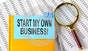 START MY OWN BUSINESS text on sticker on notebook with magnifier and chart. Business concept