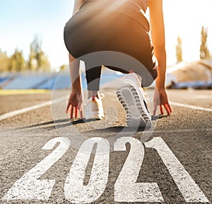 Start new year with fresh vision and ideas. Sporty woman ready for running near 2021 numbers on road, closeup