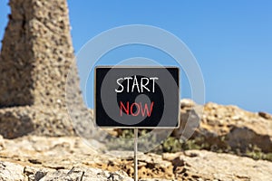 Start now symbol. Concept words Start now on beautiful black chalk blackboard. Beautiful brown stone blue sky background. Business