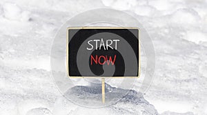 Start now symbol. Concept words Start now on beautiful black chalk blackboard. Beautiful white snow background. White snow.