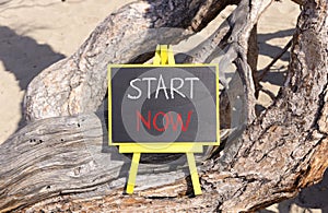 Start now symbol. Concept words Start now on beautiful black yellow blackboard. Beautiful tree background. Business marketing,