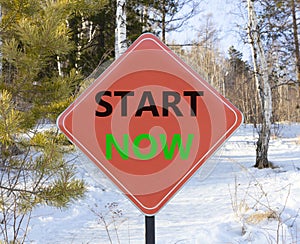 Start now symbol. Concept words Start now on beautiful red road sign. Beautiful forest snow blue sky background. Business
