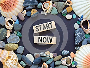 Start now symbol. Concept words Start now on beautiful wooden block. Beautiful black table black background. Sea stone sea shell.