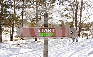 Start now symbol. Concept words Start now on beautiful wooden road sign. Beautiful forest snow blue sky background. Business