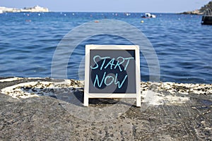 Start now symbol. Concept words Start Now on black chalk background. Beautiful sea background. Business and Start now concept.