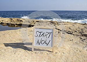 Start now symbol. Concept words Start Now on white chalk background. Beautiful sea background. Business and Start now concept.