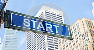 Start road sign, blue color. Highrise buildings and blue sky background