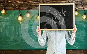 Start of school year concept. Teacher holds chalkboard in front of face. Man welcomes students, chalkboard on background