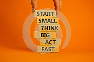 Start small think big symbol. Words `Start small think big act fast` on wooden blocks on a beautiful orange background.
