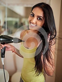 The start to a great hair day. Portrait of a young woman blowdrying her hair in the bathroom.