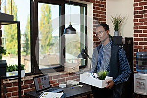 Start up employee getting fired looking sad holding tray with personal belongings leaving office