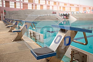 Starting blocks in row by the swimming pool, selective focus. Jump platform for swimming in swimming pool and grandstand backgroun