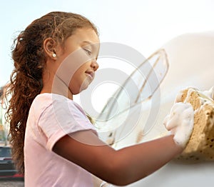 Starting chores from early childhood. Shot of a young girl washing a car outside.