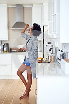 Starting her day her favourite way. Shot of a relaxed young woman eating breakfast while standing in her kitchen at home