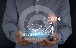 Startup business goals trend 2024 concept. Businessman holding tablet and icon rocket are launching out from screen