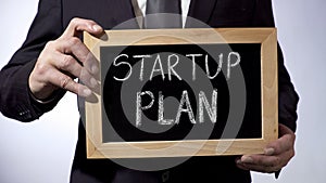 Startup plan written on blackboard, businessman holding sign, business concept