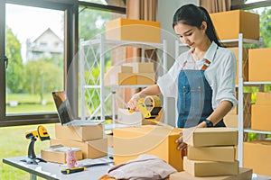 Startup small business owners holding packing machine and sealing cardboard boxes with tape to deliver products to customers-