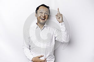 Starving Asian man wearing white shirt, pointing at the copy space on top of him, isolated by white background