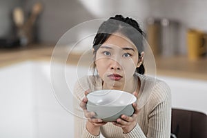 Starving asian woman holding empty plate next to mouth