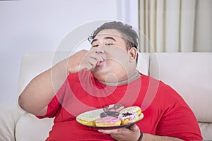 Starving fat man eating a plate of donuts at home