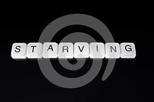 Starving,text word title caption label cover backdrop background. Alphabet letter toy blocks on black reflective