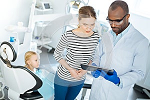 Pleasant dentist showing dental X-ray to mother of his patient
