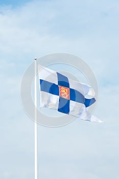 State flag of Finland with national coat of arms against blue sky