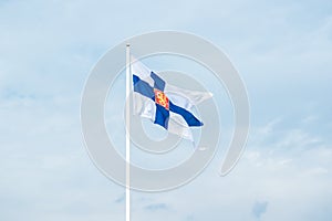 State flag of Finland with national coat of arms against blue sky