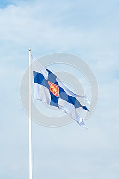 State flag of Finland with national coat of arms against blue sky